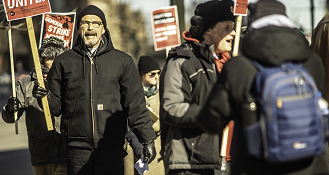 Workers on a picket line holding strike signs in winter weather
