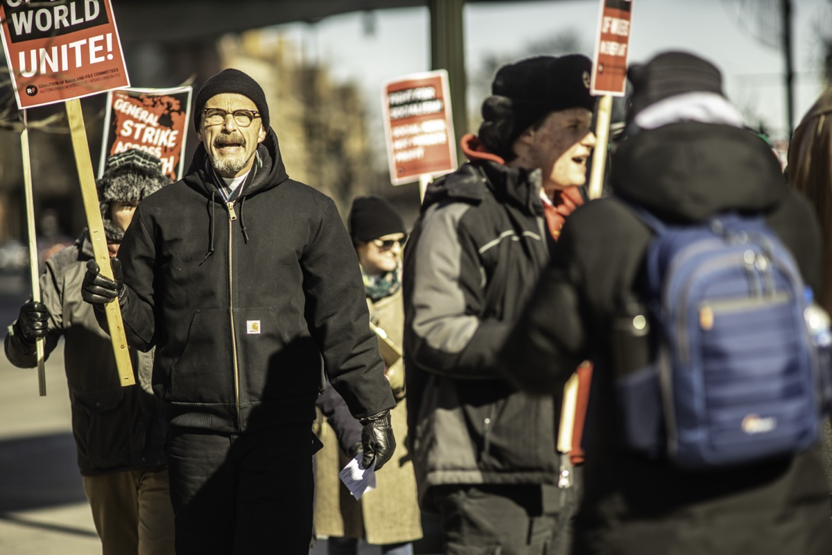 Workers on winter picket line holding WORKERS OF THE WORLD UNITE signs
